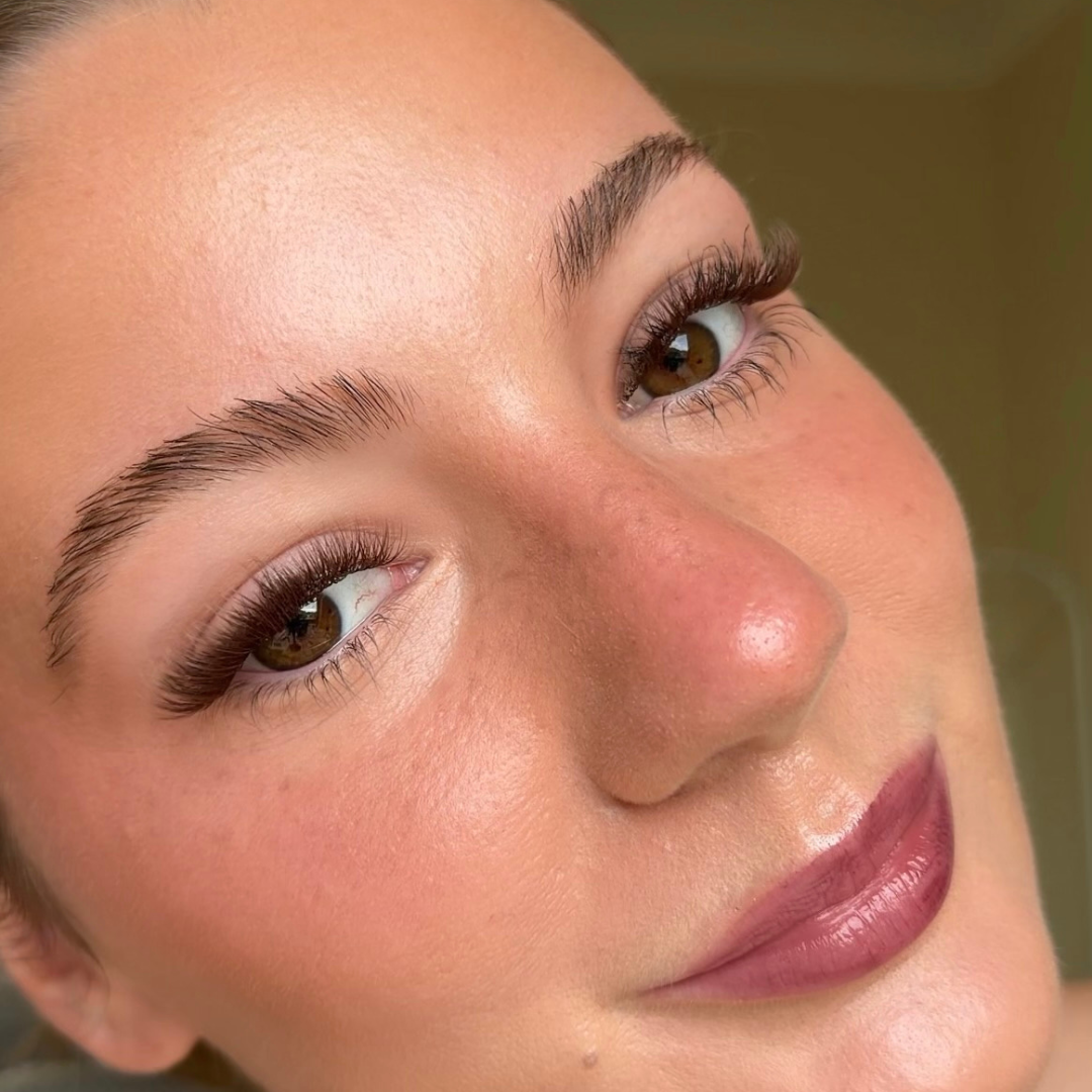 Close-up of a woman's face with brown eyes and purple lipstick, wearing brown eyelashes
