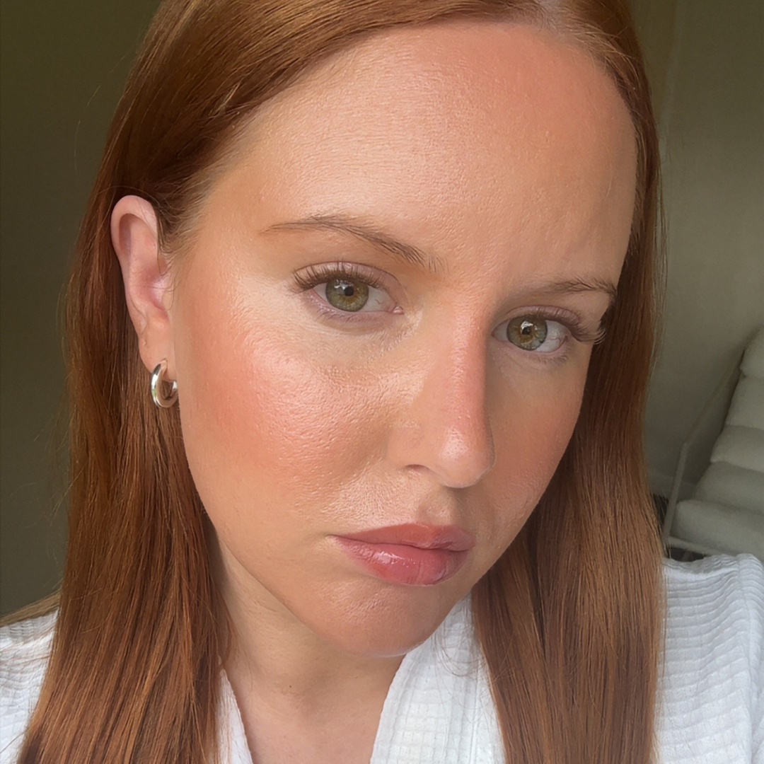 Close-up of a woman with long brown hair wearing a white shirt.
