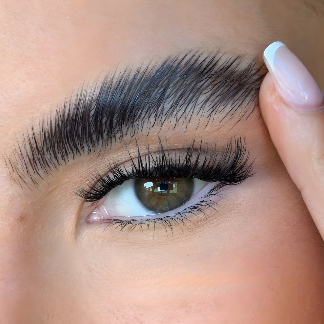 Close-up of an eye with long, thick eyelashes and a hand touching the eyebrow.